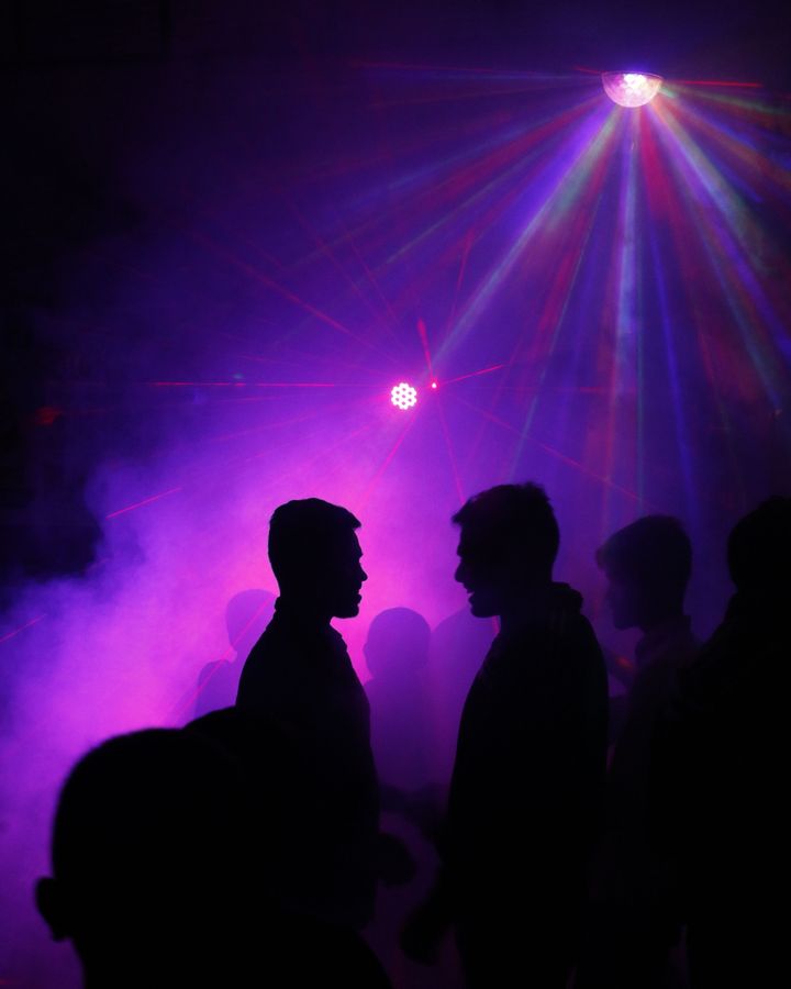 Siluetas de personas socializando bajo luces moradas de neón